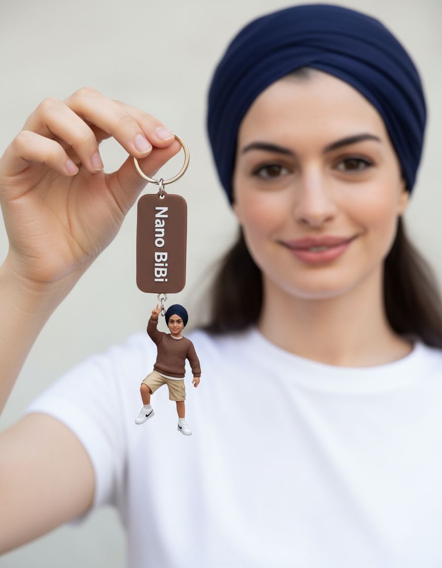 A sikh woman ( exactly matched face) holds a keychain in the shape of a miniature of herself. The miniature is very realistic, wearing a brown sweater, beige shorts, and white Nike shoes.  The miniature stands on its palms, raising its right hand in a peace sign pose. The keychain is brown with the word 'Nano BiBi' written in white. The background is blurred with a smiling real woman wearing the same white t-shirt, so the miniature looks identical to her.